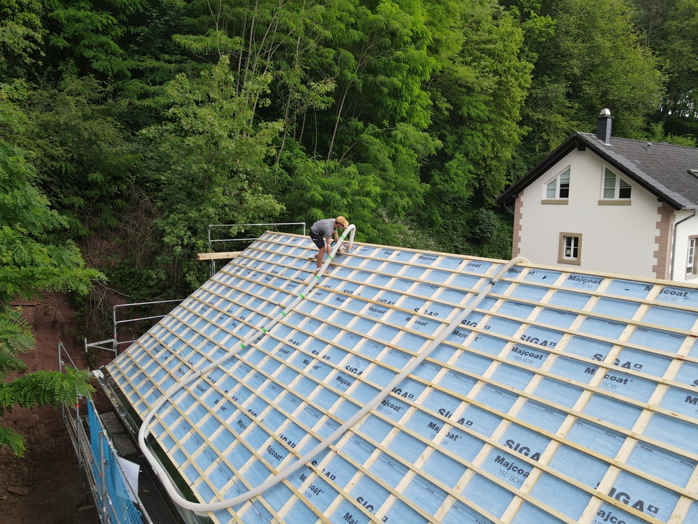 Construction workers on a roof installing blue insulation boards on a white house surrounded by trees